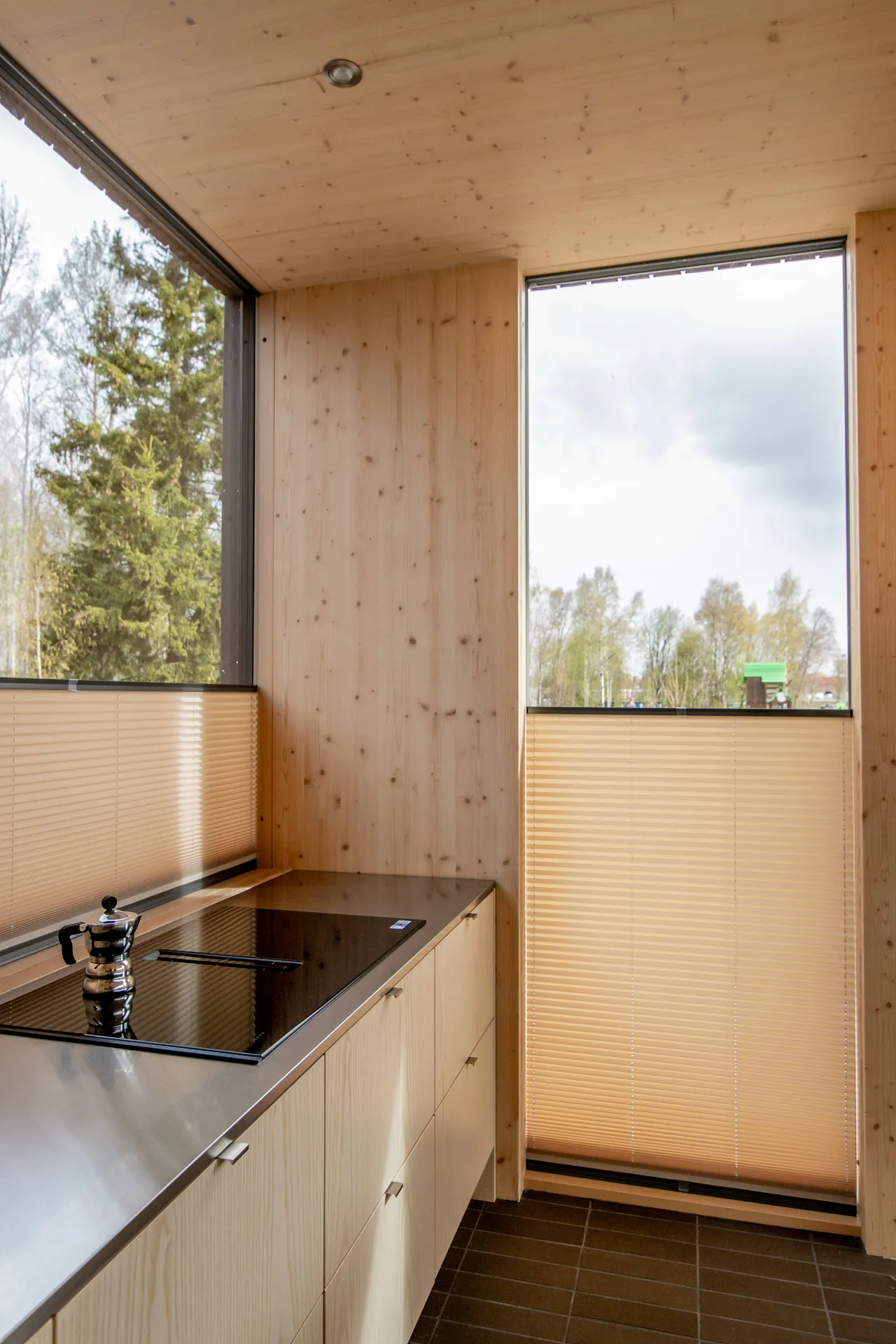 Hiekan sävyiset Visor-vekkikaihtimet peittävät puupintaisen keittiön kulmaikkunoiden alaosia.