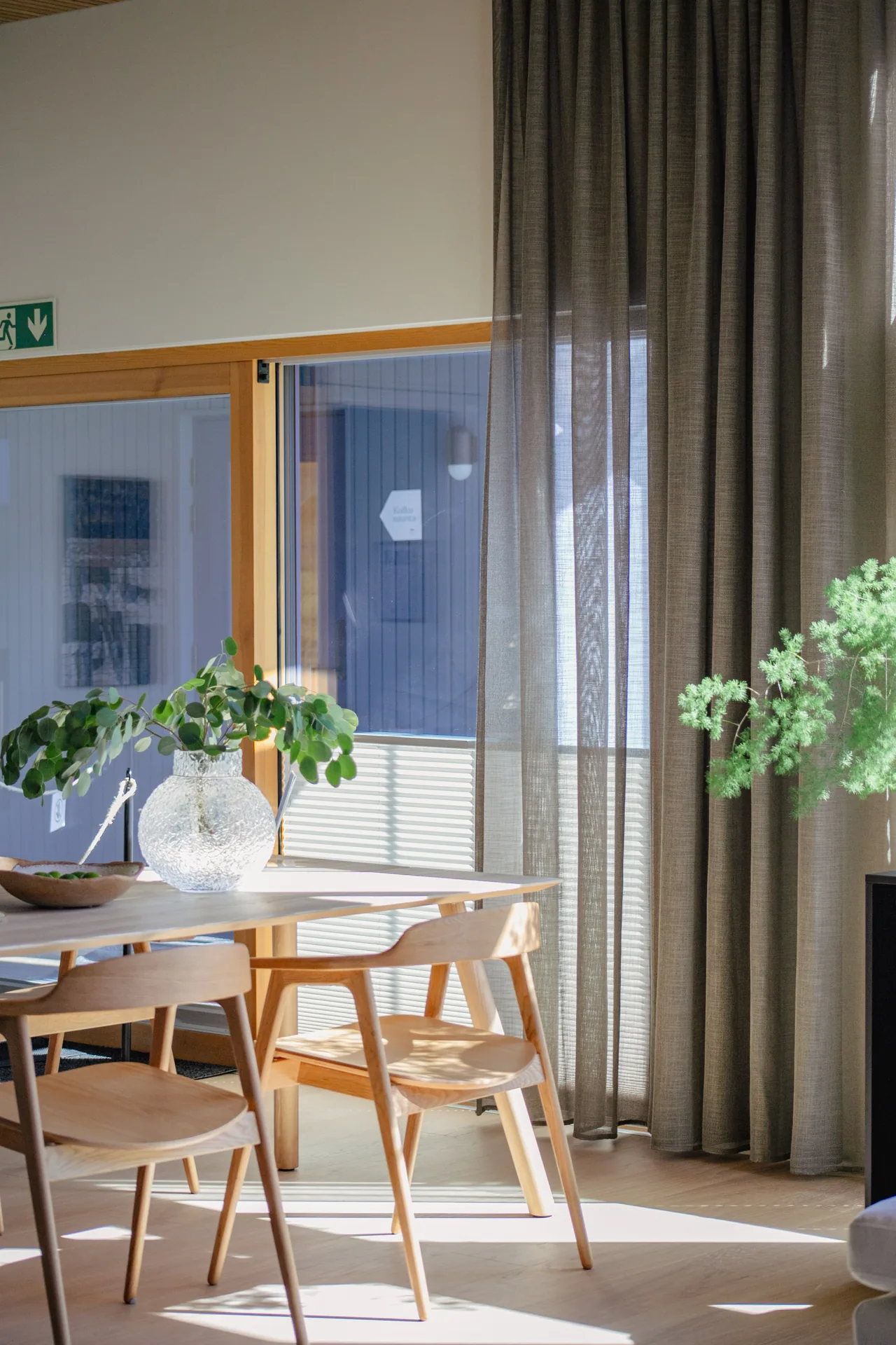 Harmaan sävyiset Visor-vekkikaihtimet suojaavat puukalusteisen ruokailuhuoneen suuria ikkunoita.